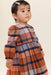 Young child wearing a Pink Chicken long sleeve plaid dress in warm rust blue and cream tones with a gathered skirt and hair clip posing indoors