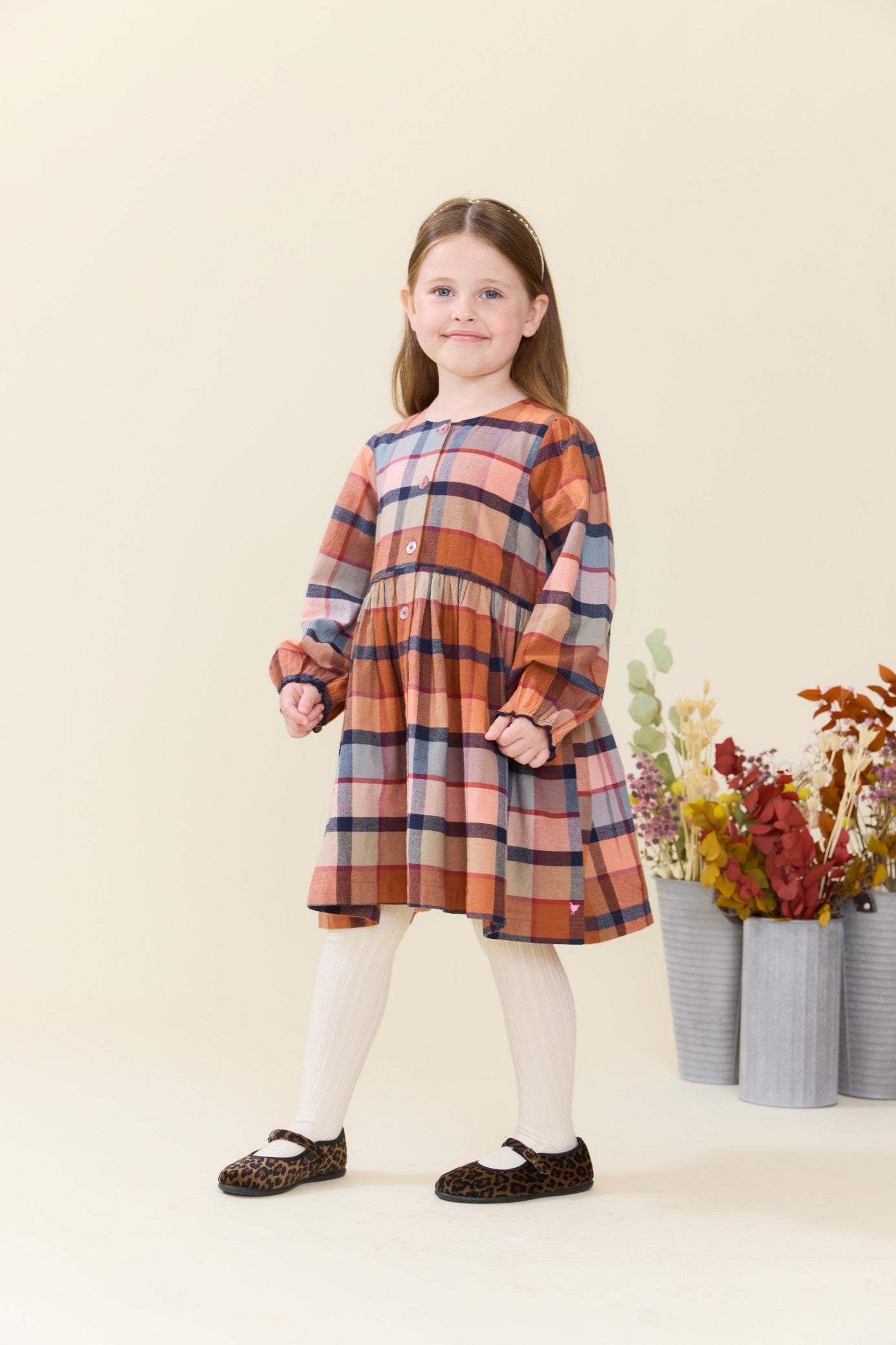 Young girl modeling a Pink Chicken plaid long sleeve dress with white tights and leopard print shoes in a bright studio setting