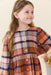 Young girl wearing a warm brown and navy plaid dress with button details and a gathered skirt from Pink Chicken