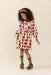 Young girl wearing a long sleeve cream dress covered in colorful hearts with a pink headband olive socks and brown shoes from Pink Chicken
