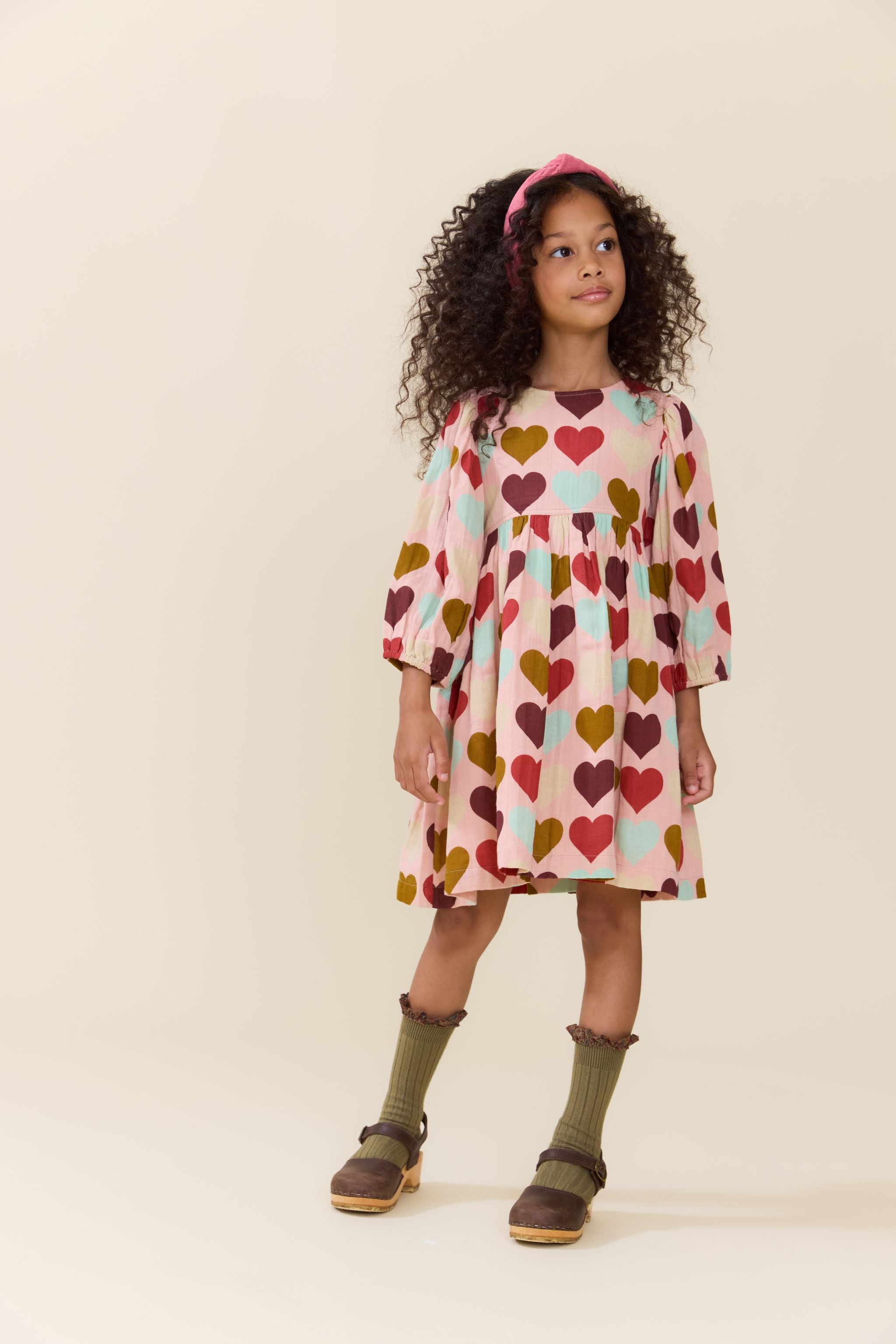 Pink Chicken girls dress in a pink and cream heart print with three quarter sleeves modeled by a child with curly hair and boots