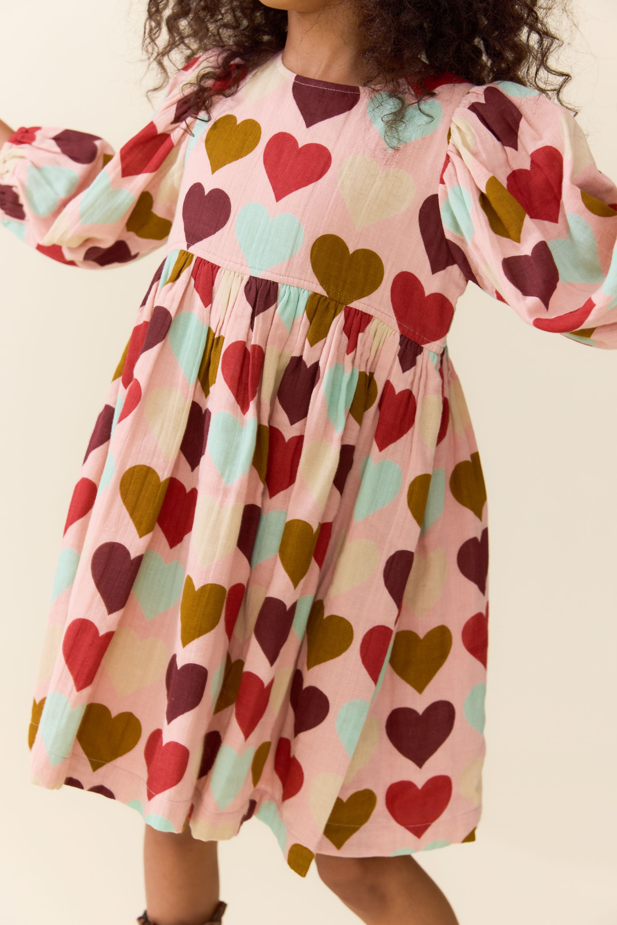 Child wearing a pink dress with colorful heart print and puff sleeves by Pink Chicken