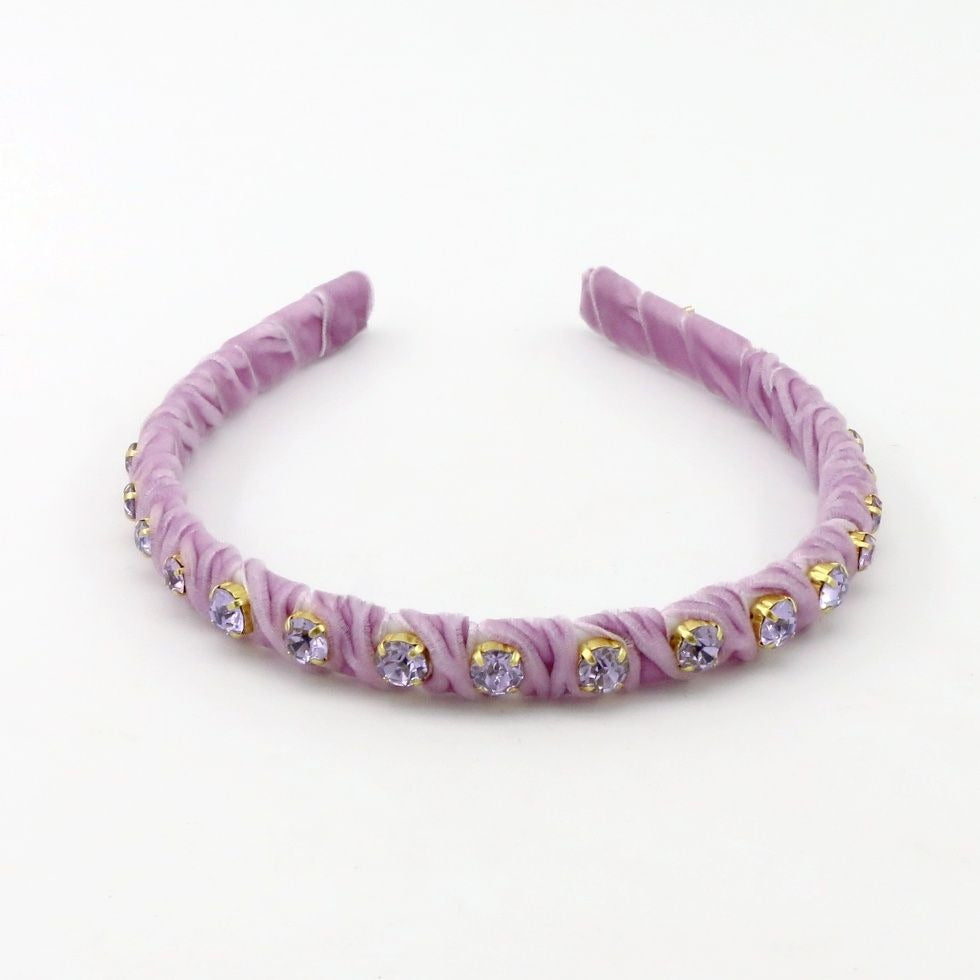 A lavender purple fabric headband with ruched rosettes and small gold-rimmed clear rhinestones, displayed on a clean white background.