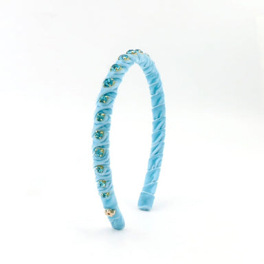 A light blue velvet headband decorated with small blue and green rhinestone clusters and a gold-tone bow at the front, shown on a plain white background.