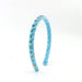 A light blue velvet headband decorated with small blue and green rhinestone clusters and a gold-tone bow at the front, shown on a plain white background.