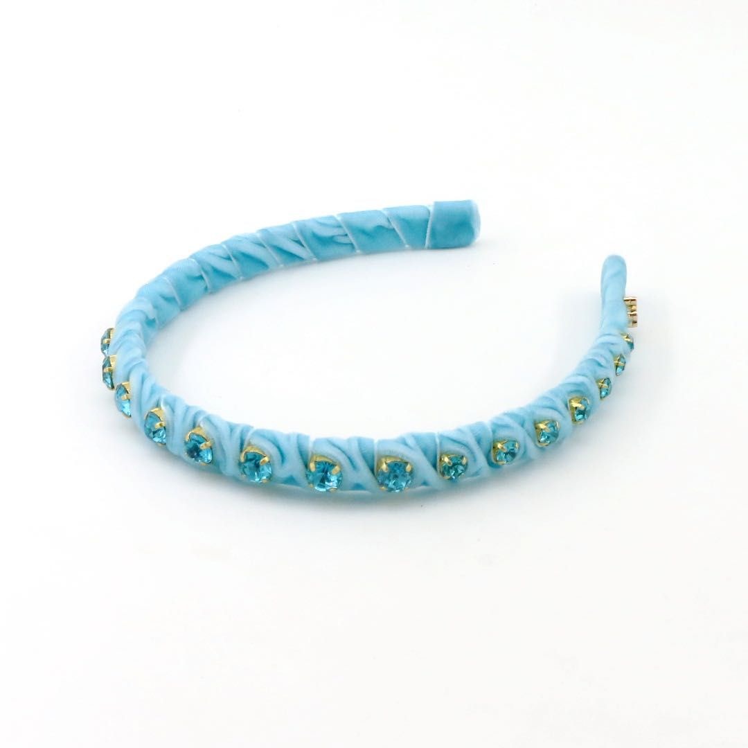 A light blue velvet headband decorated with small gold rhinestone accents and blue crystals, displayed on a clean white background.