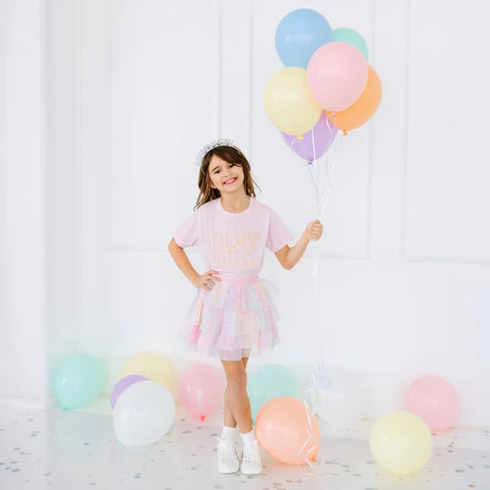 Young girl in a pastel dress holding colorful balloons against a white background