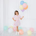 Young girl in a pastel dress holding colorful balloons against a white background