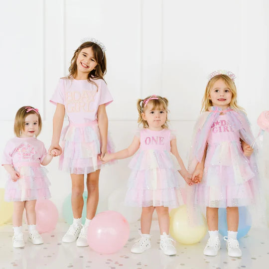 Four young girls in matching dresses with text, standing in a line against a white background.