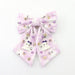 A light purple and white hair bow decorated with small rhinestones, pearl-like beads, and cute Halloween ghosts on a plain white background.