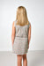 A young girl with long blonde hair is shown from behind, wearing a sleeveless dress with a dense multicolor floral pattern on a light beige background with white trim.