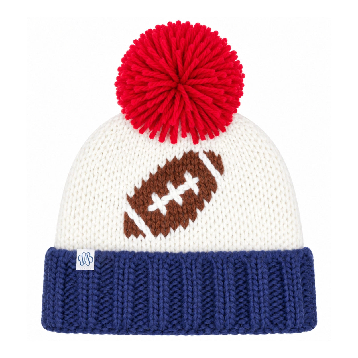 A white knit beanie with a red pom-pom on top, a brown football motif with white laces on the front, and a navy blue ribbed cuff. A small white square tag with a blue monogram is visible on the cuff.