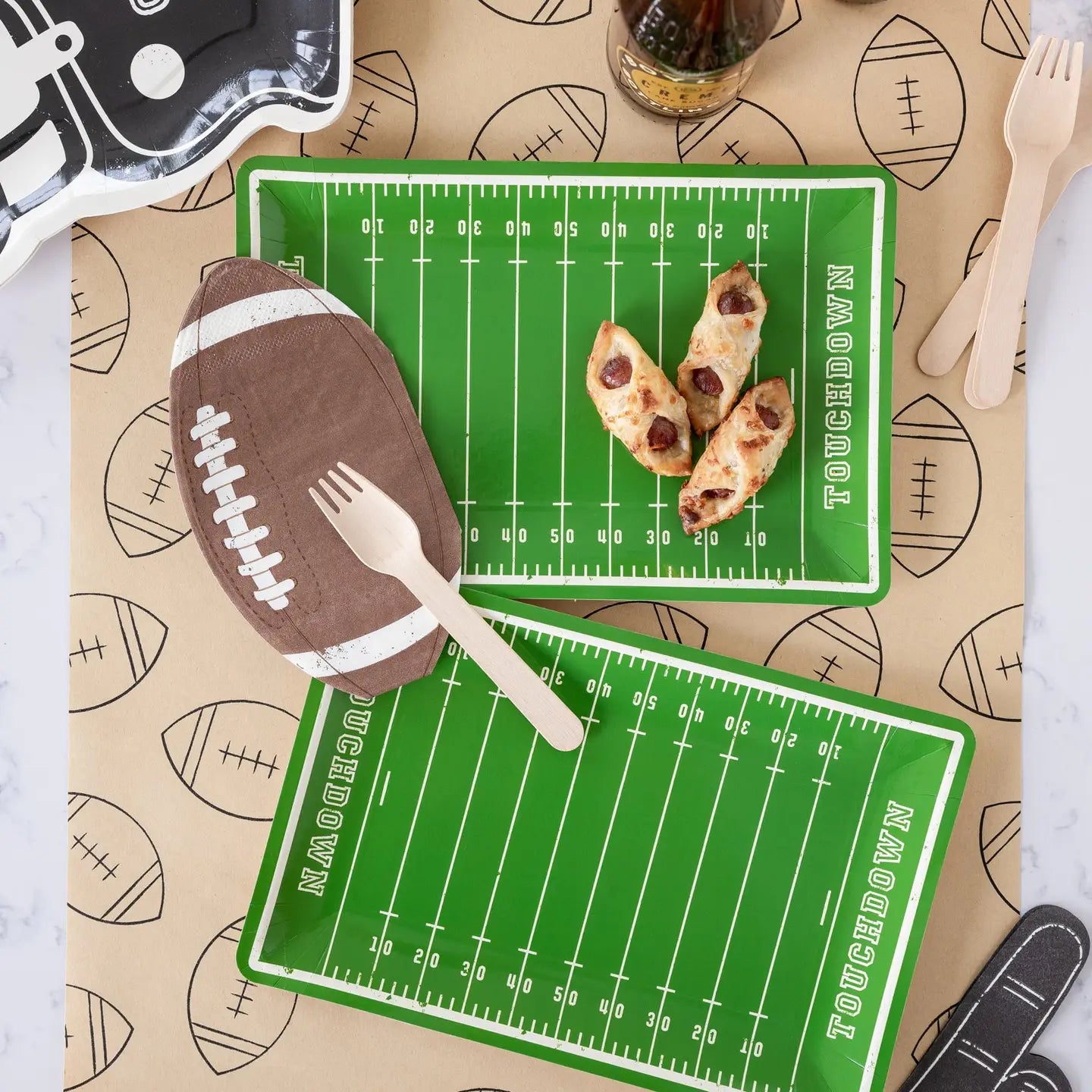 Football-themed place with food and cutlery on a tablecloth with football patterns.