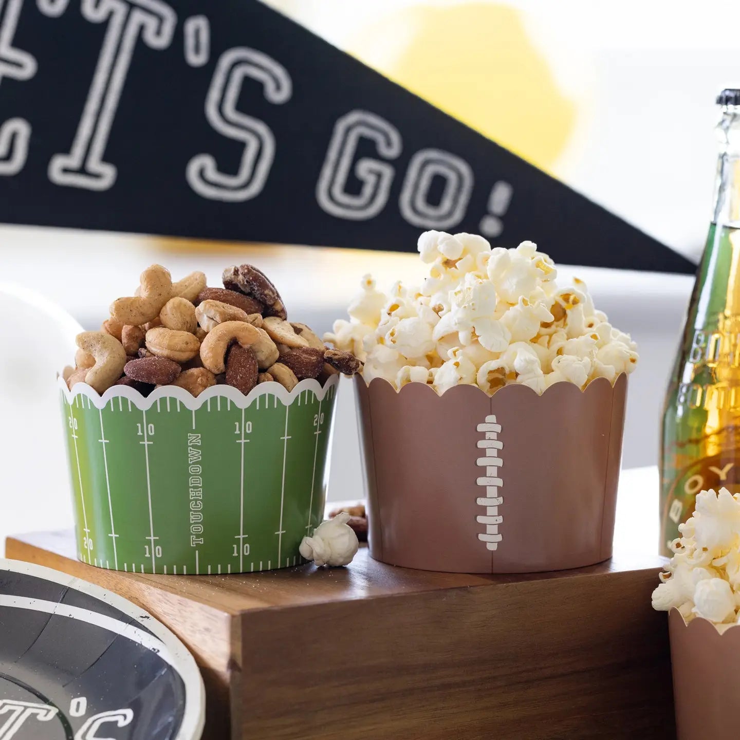 Two snack cups with popcorn and nuts on a wooden tray, with a 'Let's Go!' banner in the background.