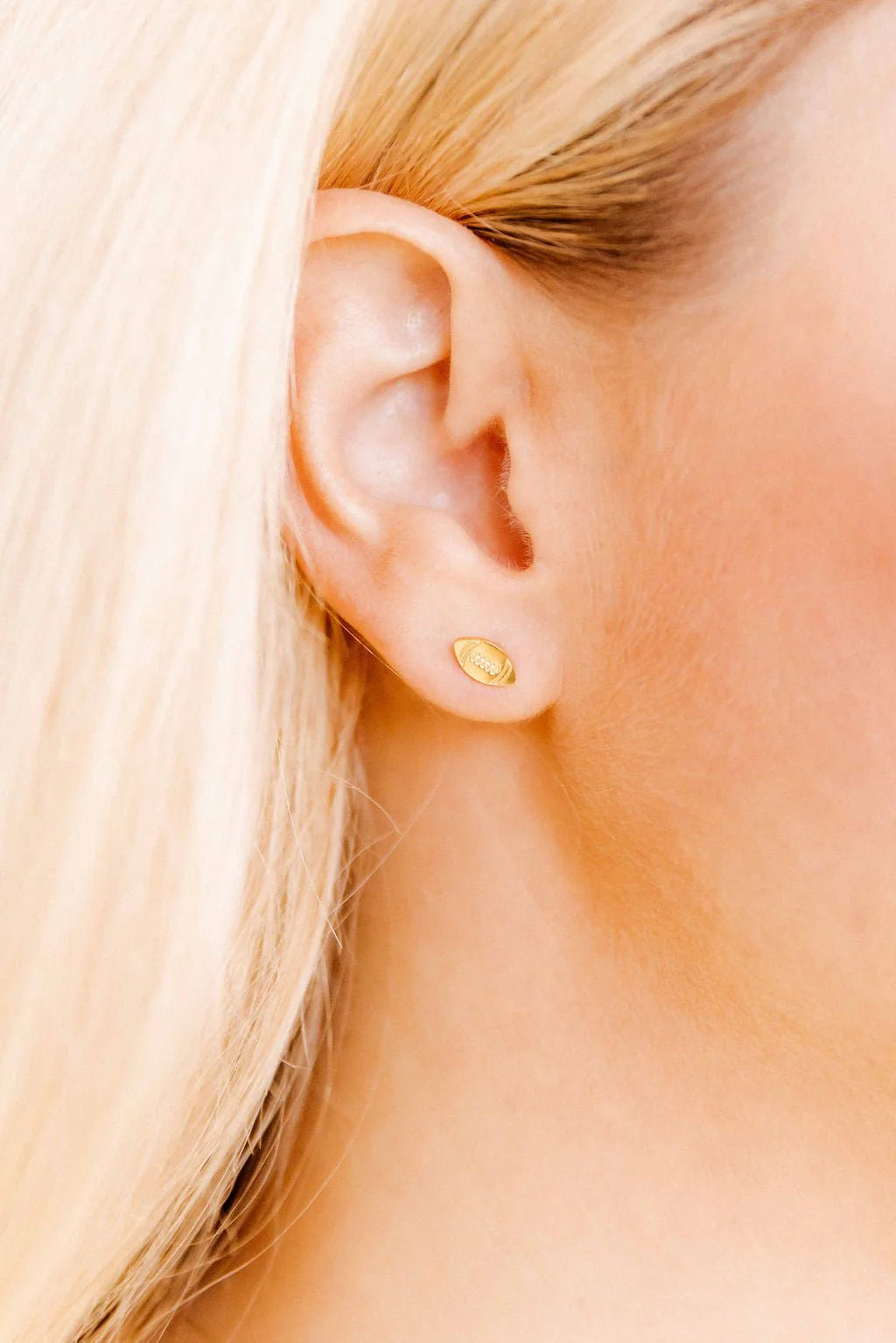 Close-up of a person wearing a gold football earring.