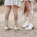 Two pairs of legs wearing shiny gold cowboy boots on a natural background.