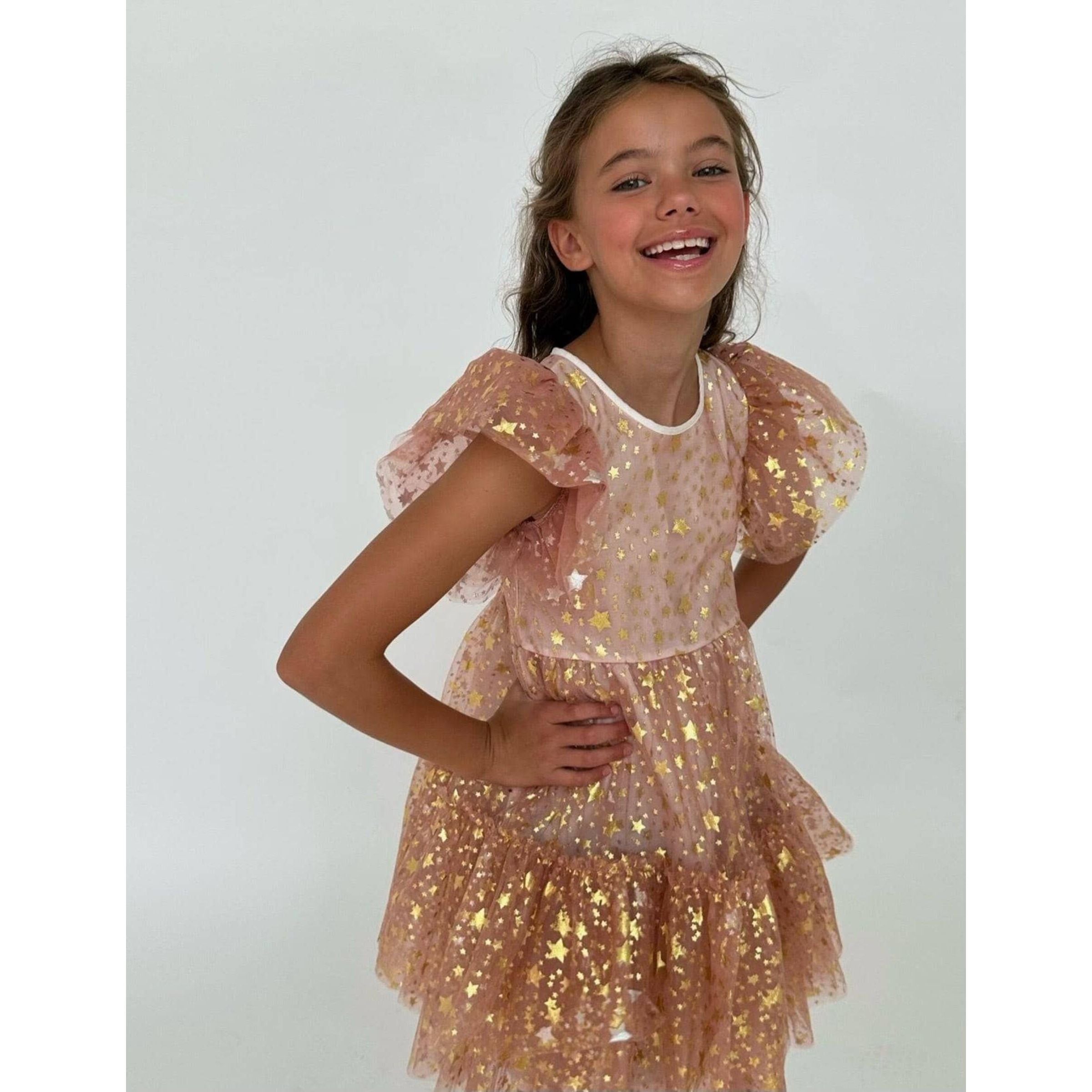 girl wearing. blush colored tulle dress covered in gold metallic stars