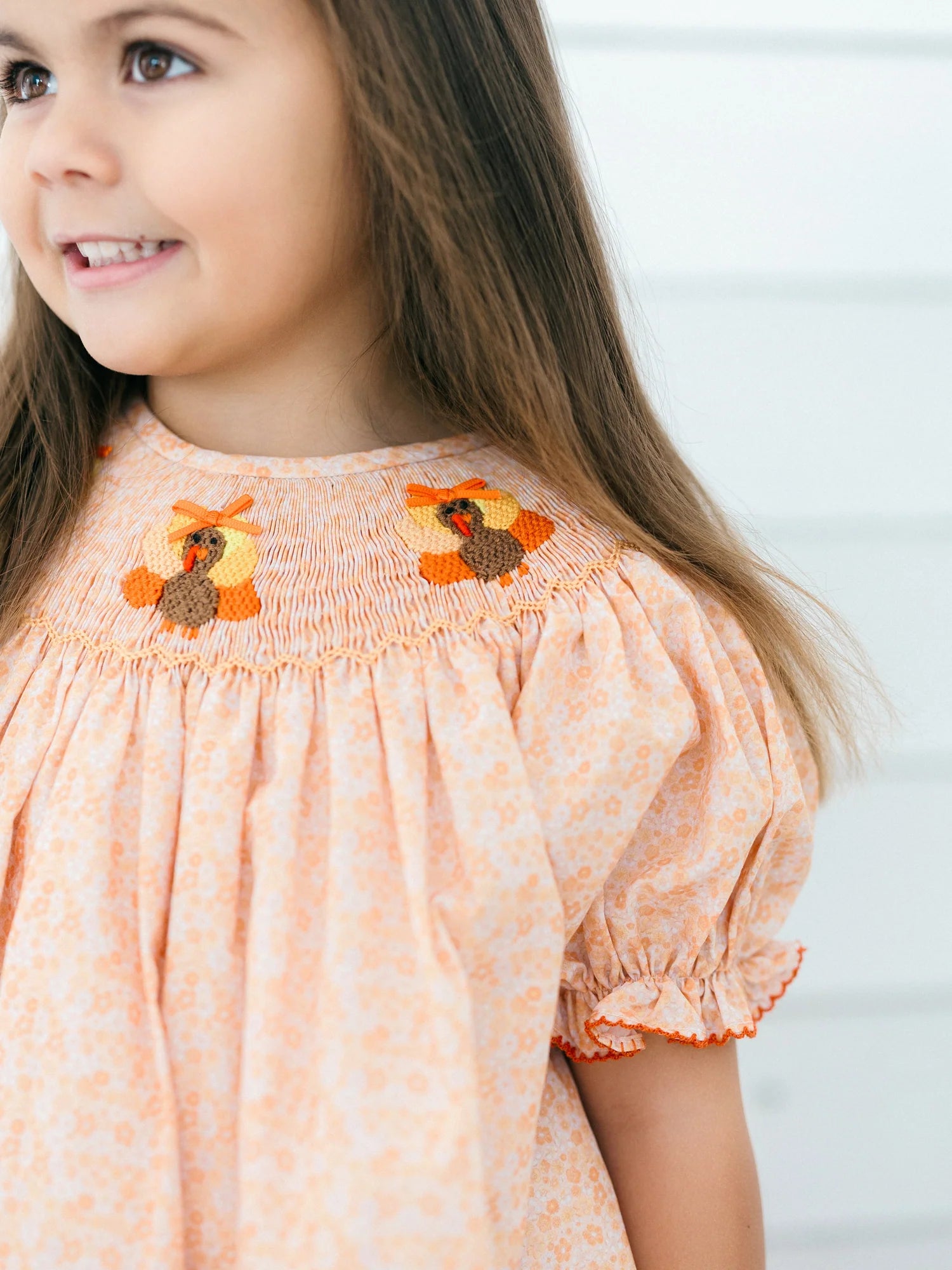Young girl wearing a peach floral dress with a smocked neckline embroidered with turkey details and short puff sleeves by Poppy Kids