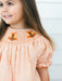 Young girl wearing a peach floral dress with a smocked neckline embroidered with turkey details and short puff sleeves by Poppy Kids