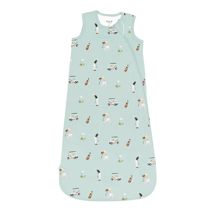 A sleeveless baby sleep sack in a light mint green color, featuring an all-over repeating print of golf players, golf carts, and golf clubs. The garment is displayed flat against a solid white background.