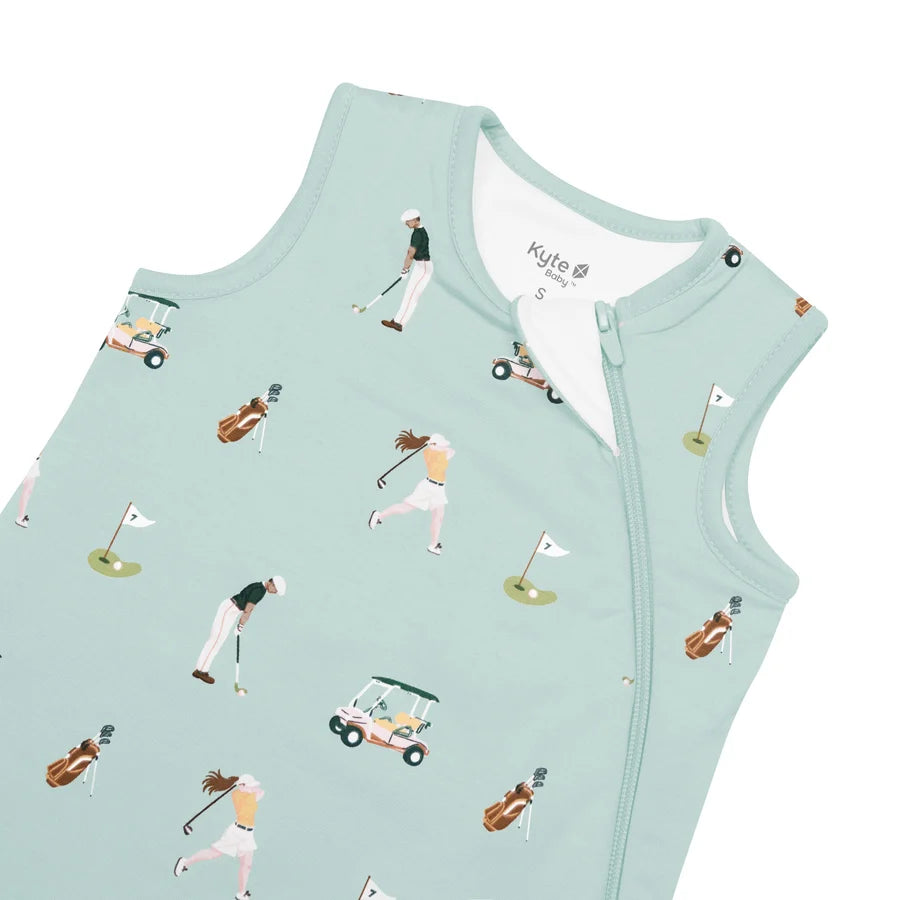 A sleeveless baby sleep sack in mint green, featuring an all-over golf-themed print with illustrated golfers, carts, and flags. The brand name 'Kylie Baby' is visible on the inner neck label.