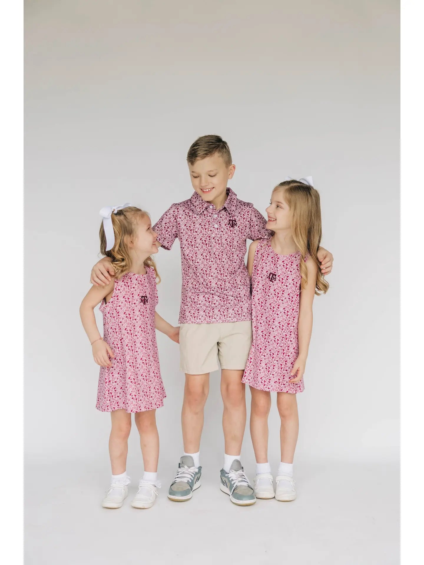 Three children wearing matching outfits with maroon A&M patterns on a white background