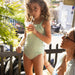Young girl in a green swimsuit holding a drink with a straw, standing next to an adult.