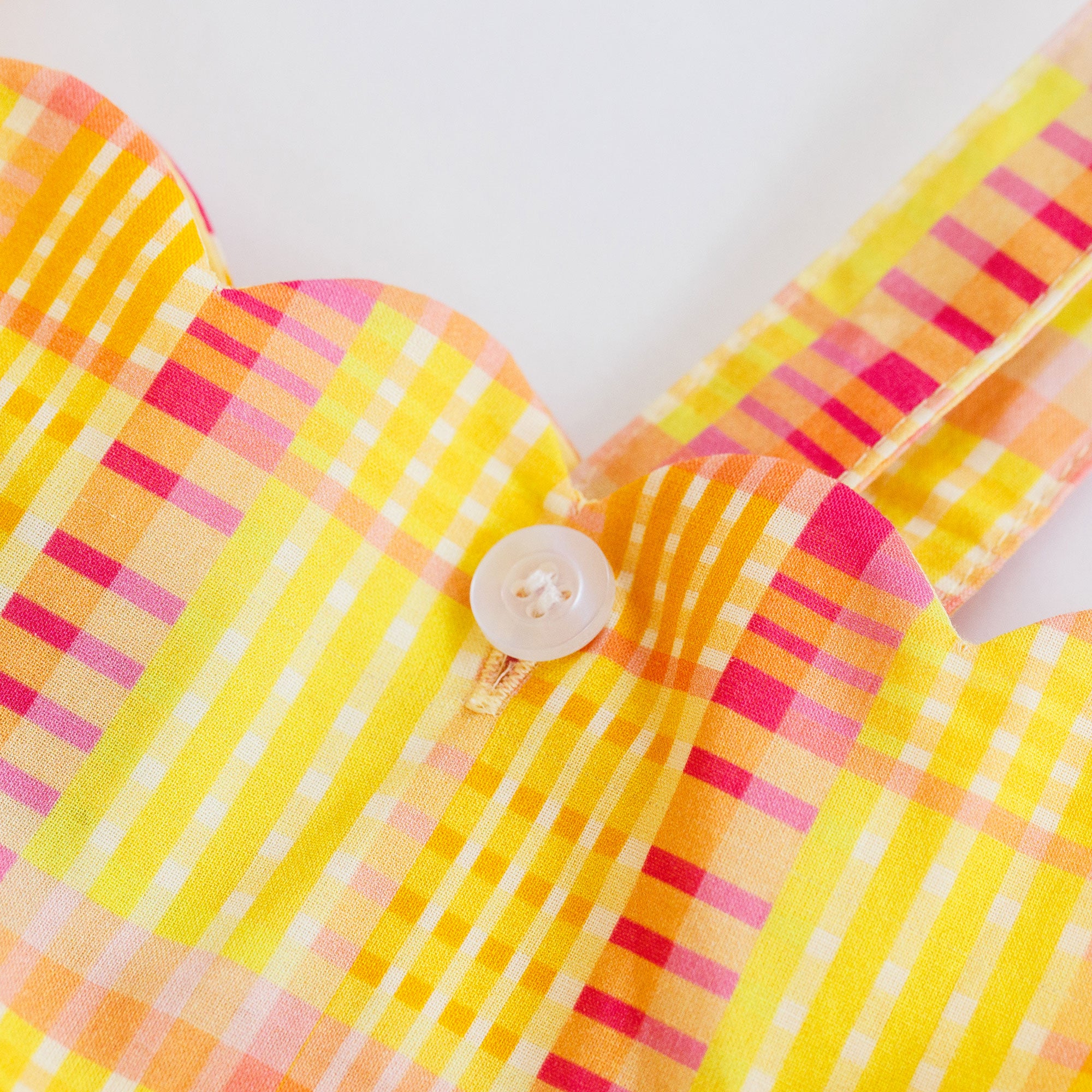 Close-up of a yellow and pink plaid fabric with a button on a white background