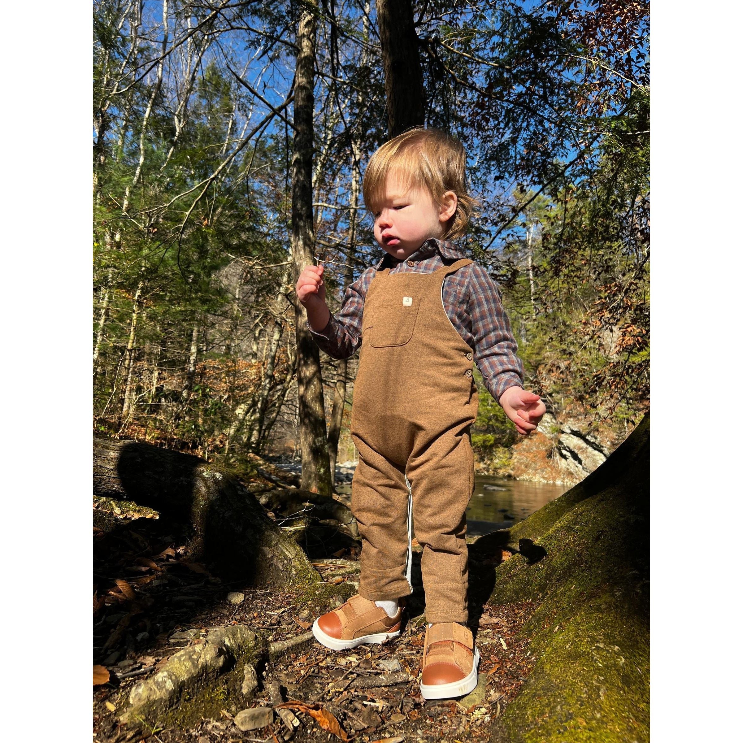 toddler boy wearing grey, blue and brown plaid collared onesie with brown overalls