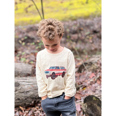 boy wearing cream colored long sleeve tee with red and off white bronco graphic with gray pants