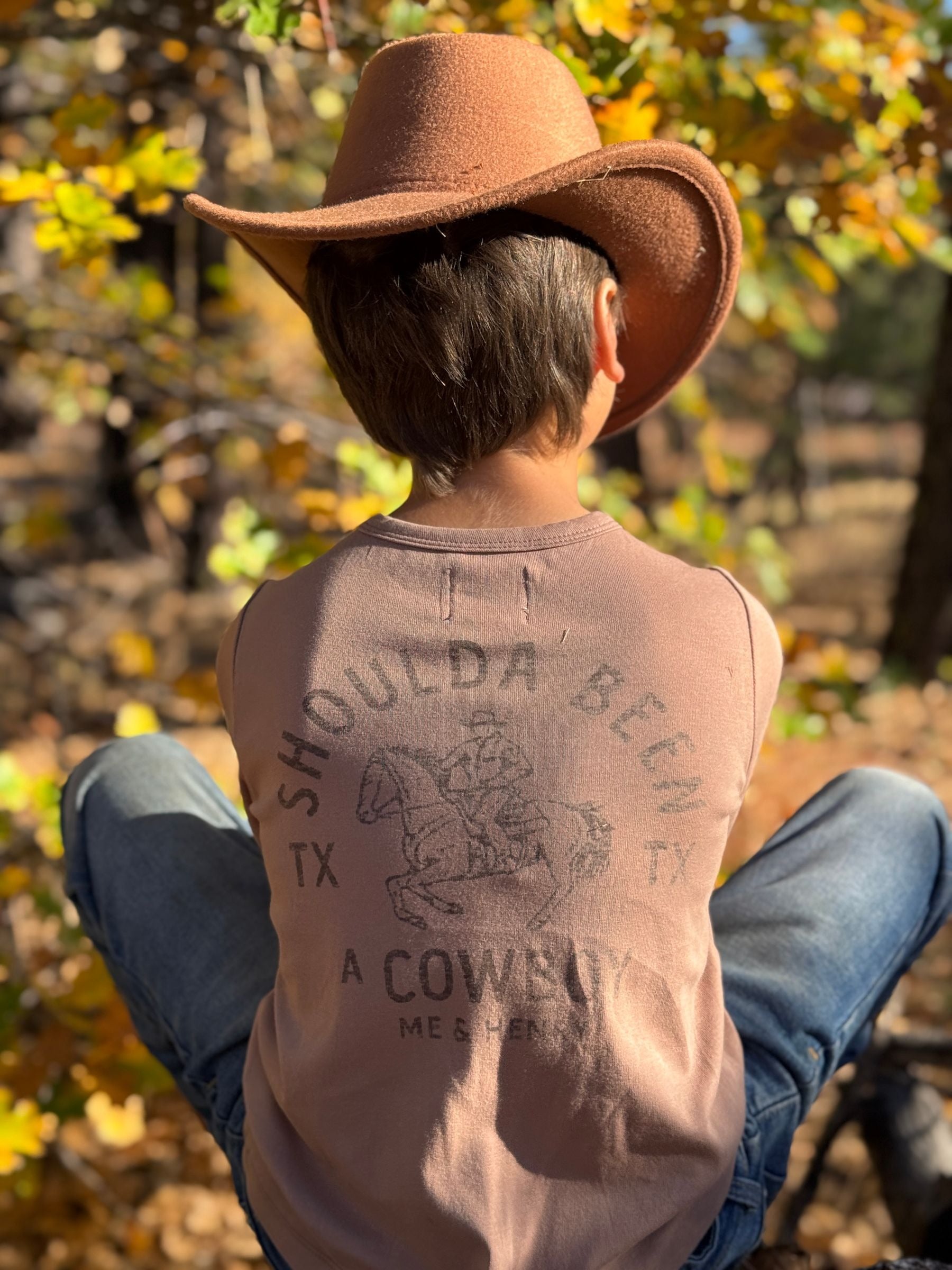 Person wearing a cowboy hat and long sleeve shirt with text sitting in a natural setting.
