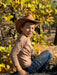 Child wearing a cowboy hat sitting among trees with autumn leaves