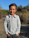 A young boy smiling outdoors, wearing a long-sleeve polo shirt with thin navy and off-white horizontal stripes, paired with dark gray jeans.