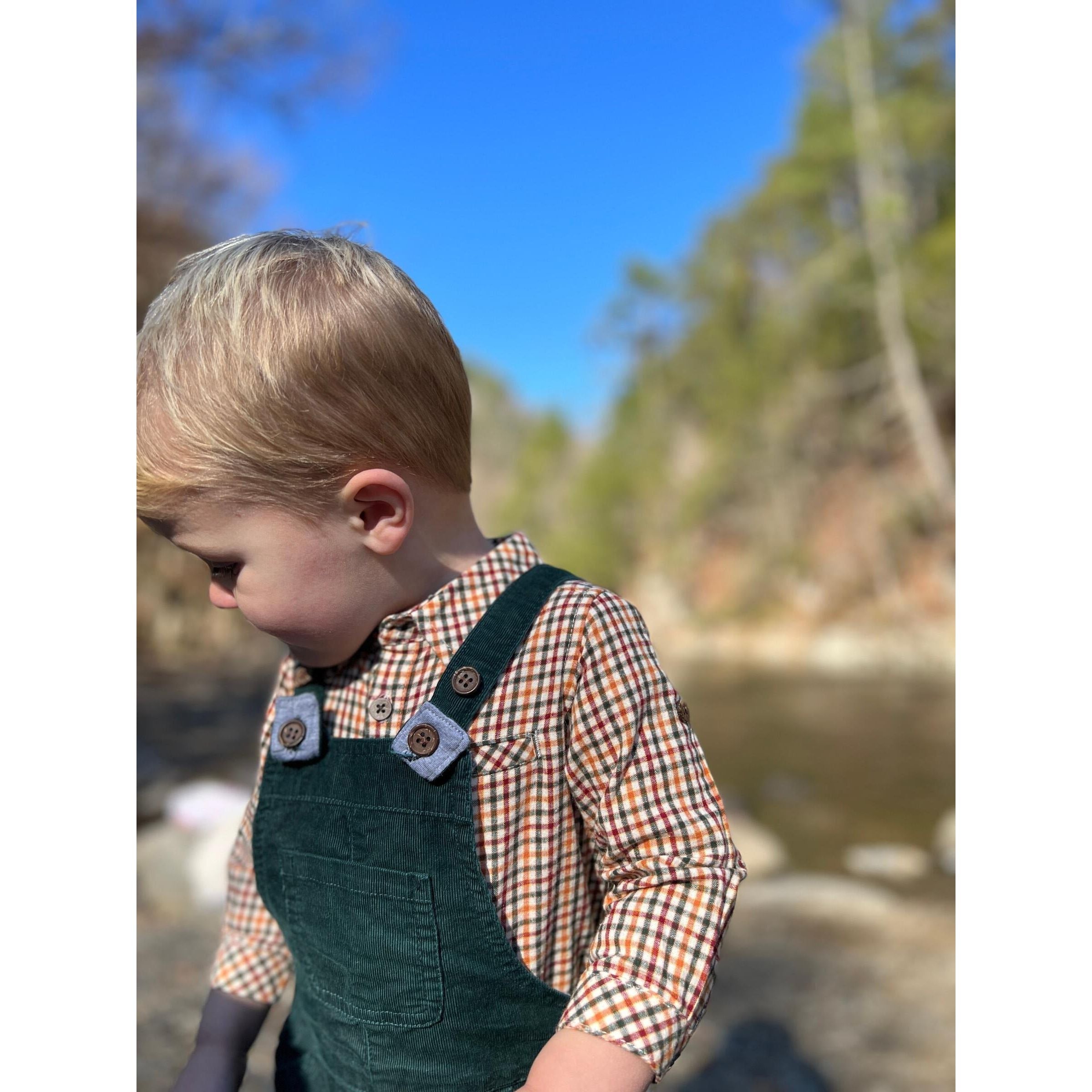 boy wearing green, red and yellow plaid long sleeve button down with green overalls