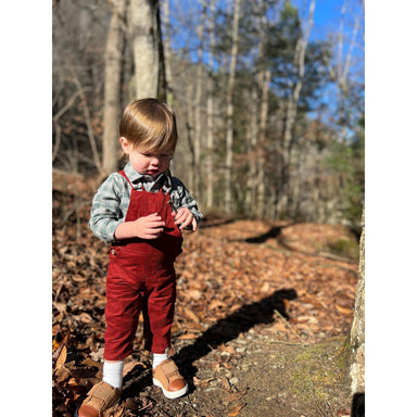 boy wearing red corduroy overalls with green and blue long sleeve button down onesie
