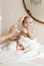 Baby being bathed with a brush and soap, wrapped in a towel on a soft surface.