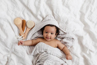 Baby wrapped in a towel with bath brushes on a white background