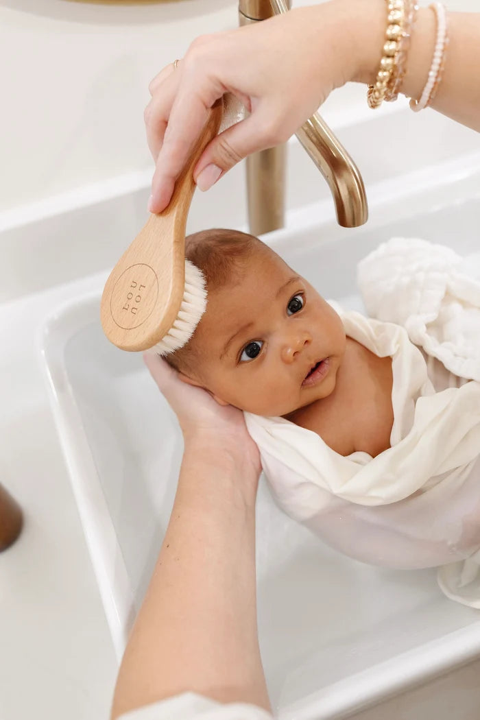 Baby being bathed with a wooden brush in a sink