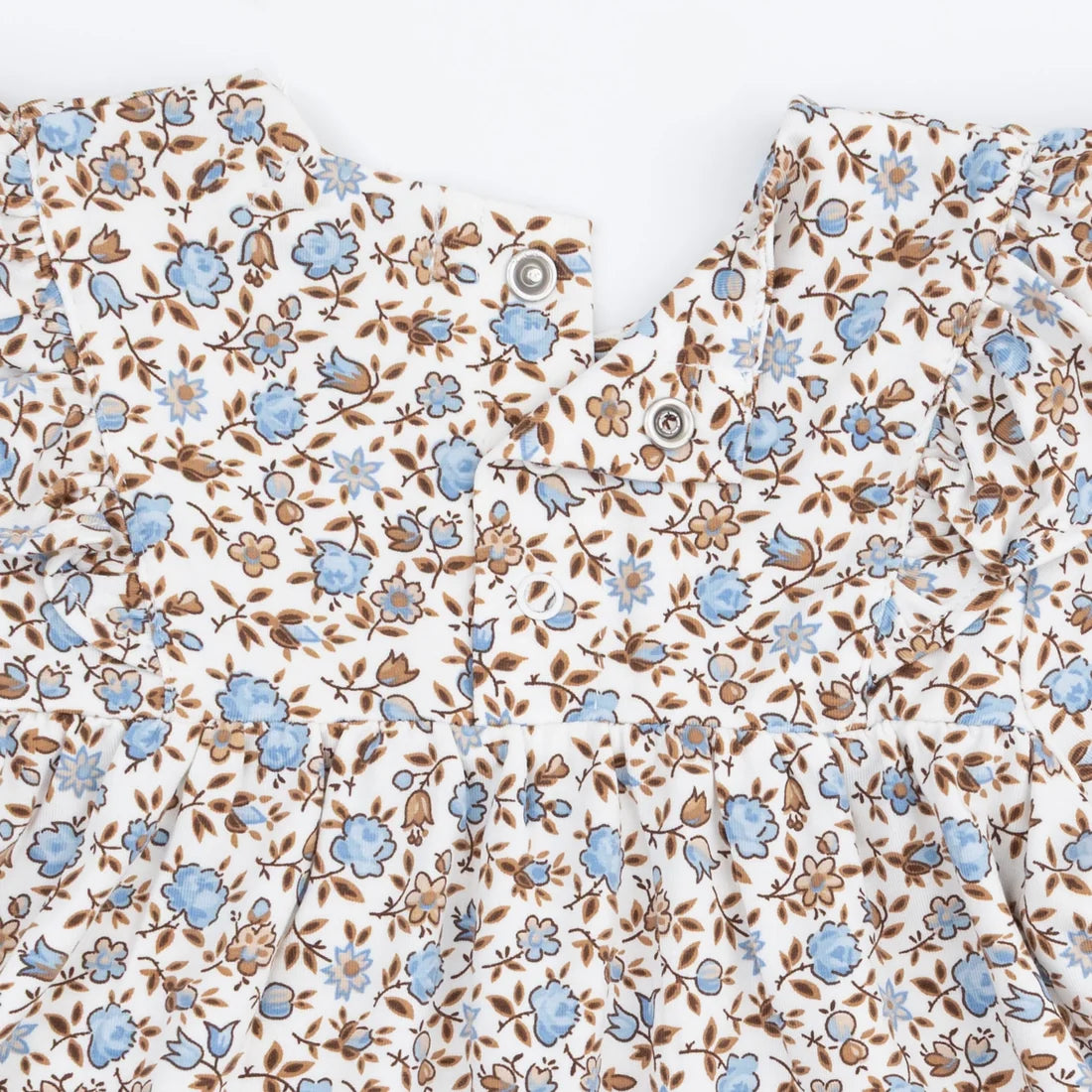 Close-up of a baby top featuring a delicate floral and bird print in light blue and brown on a warm cream background, with a snap-button neckline.