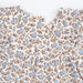 Close-up of a baby top featuring a delicate floral and bird print in light blue and brown on a warm cream background, with a snap-button neckline.