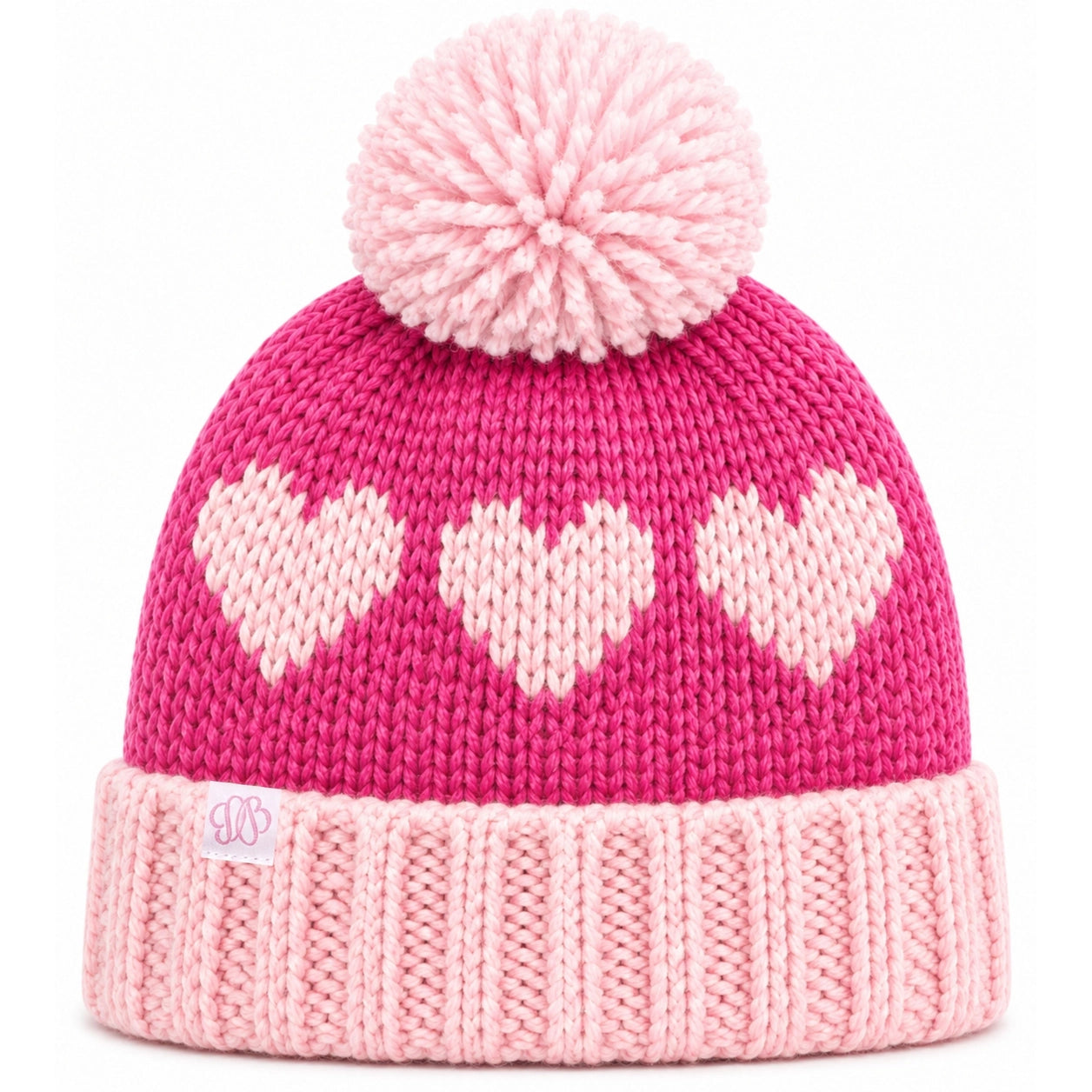 A pink knit beanie hat with a large matching pom-pom on top, featuring three light pink hearts knitted across the upper section and a ribbed light pink cuff. A small embroidered logo patch is visible on the cuff.