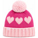 A pink knit beanie hat with a large matching pom-pom on top, featuring three light pink hearts knitted across the upper section and a ribbed light pink cuff. A small embroidered logo patch is visible on the cuff.