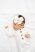 Newborn baby wearing a white outfit with gold buttons and a large bow headband on a white background