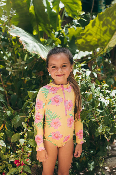 Young girl wearing a colorful swimsuit with floral patterns in a lush green outdoor setting.