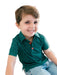 A young boy smiling and looking to the side, wearing a dark green short-sleeve polo shirt with tiny holly pattern and red buttons, paired with light blue jeans.
