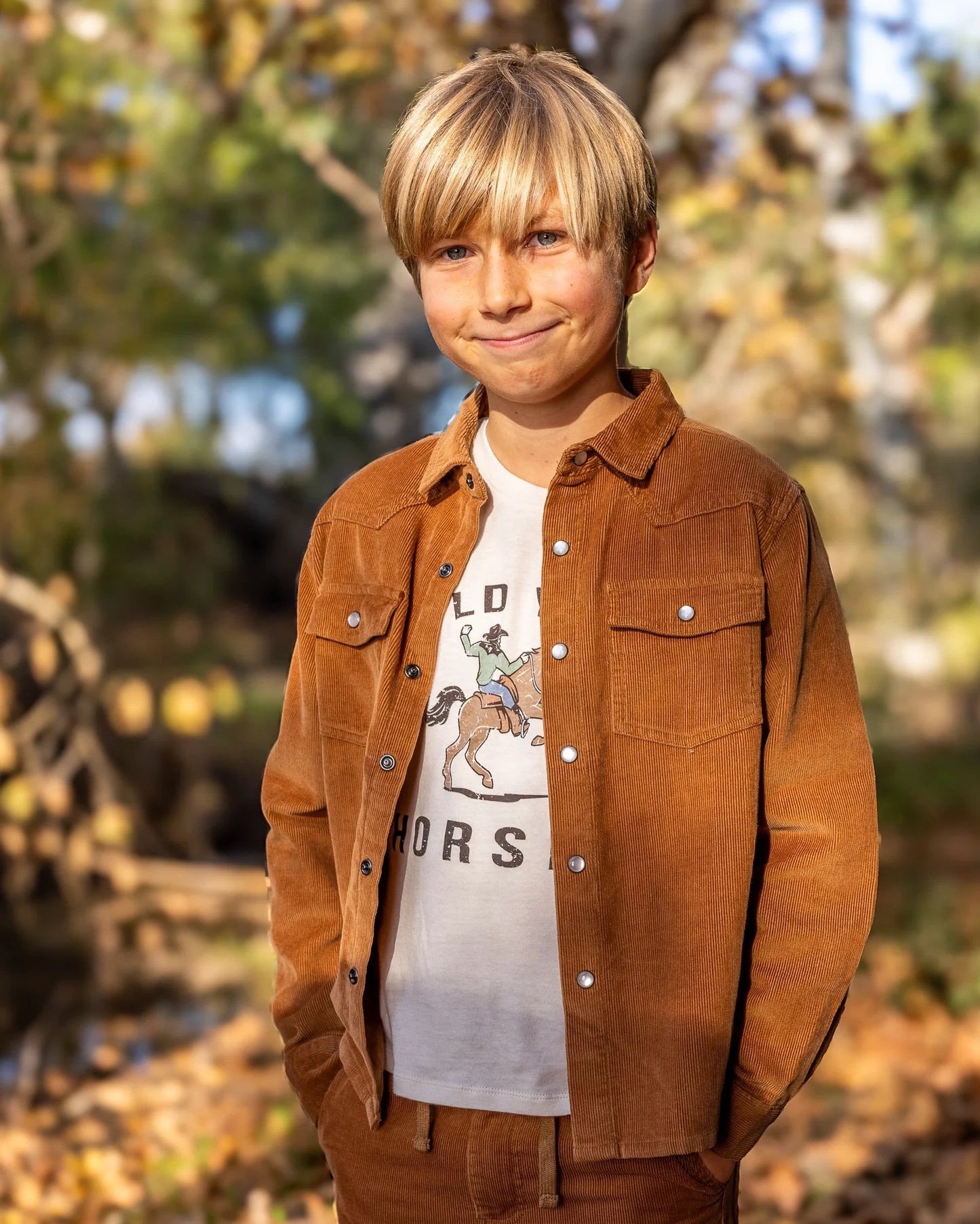 Boy wearing a Hold Your Horses tee under a brown corduroy jacket