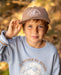 A boy wearing a snapback hat featuring brim rope and embroidered fish patch on the front panel.