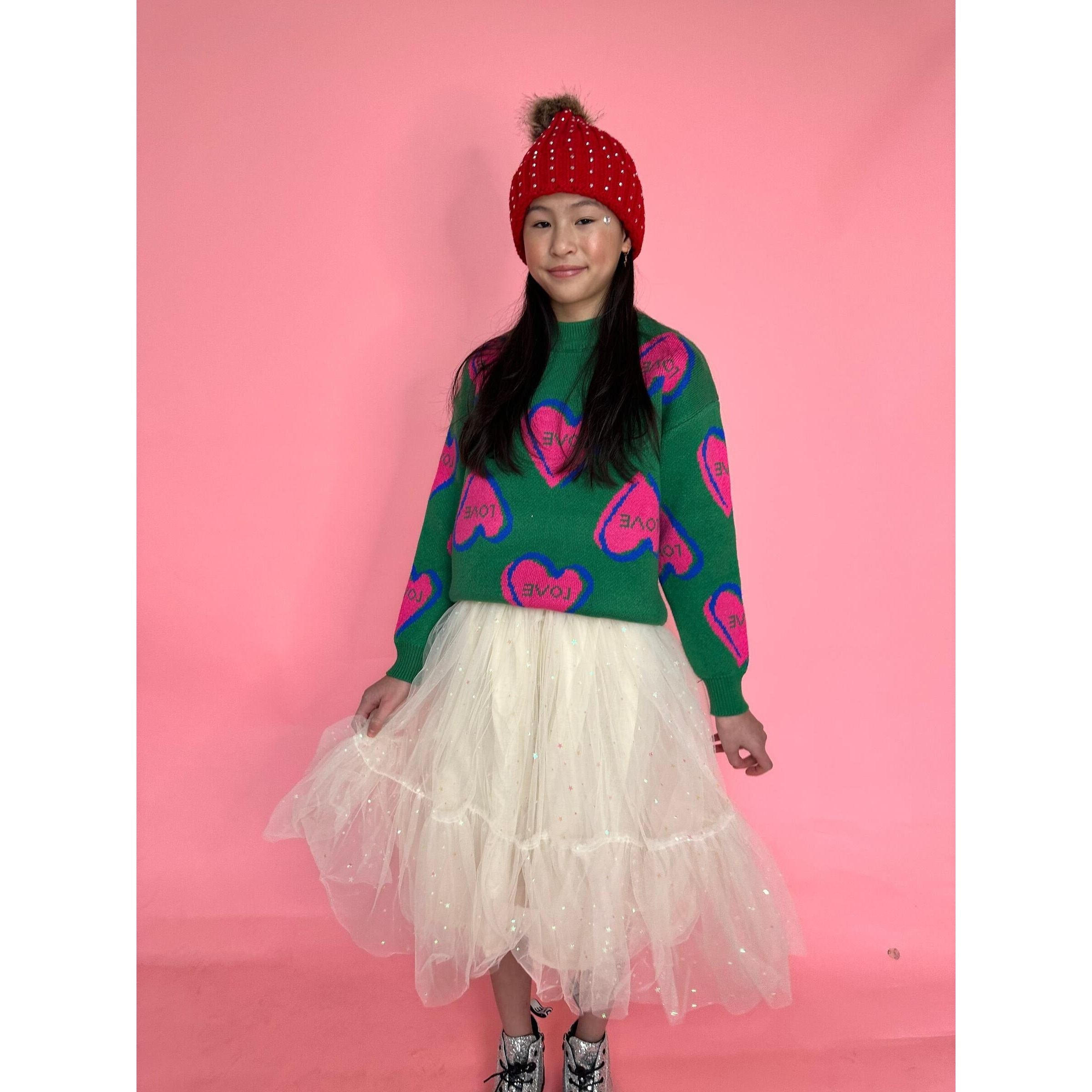 girl wearing green long sleeve sweater with knit pink and blue hearts with "love" printed inside