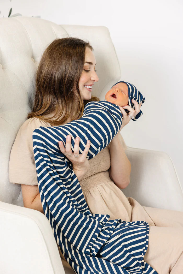 Woman holding a baby wrapped in a blue and white striped knotted gown on a white couch.