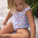 Child wearing a colorful floral swimsuit sitting on a stone surface.